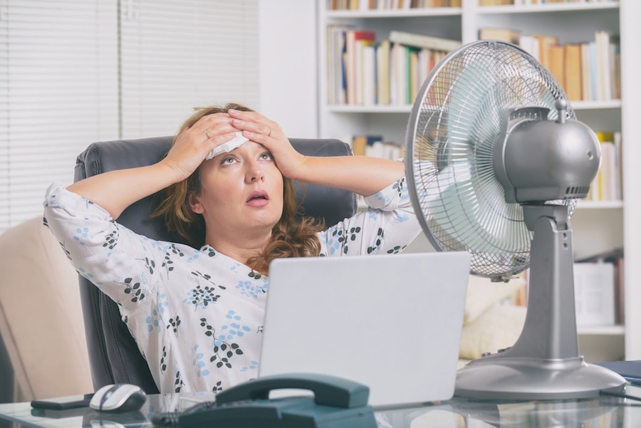 Woman suffers from heat while working in the office and tries to cool off by the fan