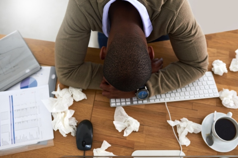 AC and Allergies - High angle shot of a young businessman feeling ill at his work desk.